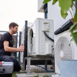 Technician Servicing Outdoor Air Source Heat Pump Unit Near House Wall
